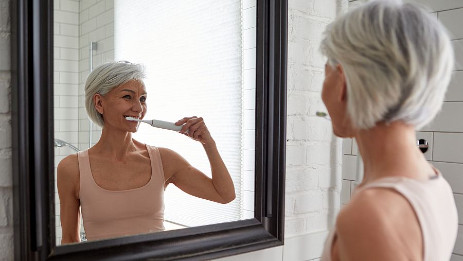 Una señora se cepilla los dientes frente al espejo