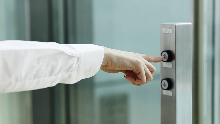 Imagen de una botonera de ascensor y un brazo que pulsa el botón de llamada
