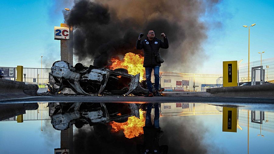 Un manifestante frente a un automóvil en llamas