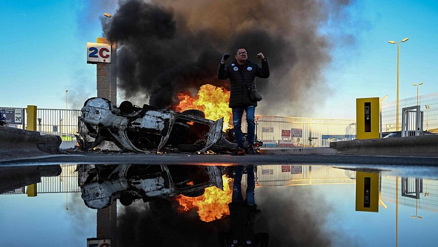 Un manifestante frente a un automóvil en llamas