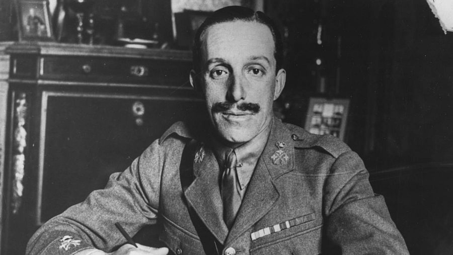 El rey Alfonso XIII sentado en su mesa de despacho mirando a cámara