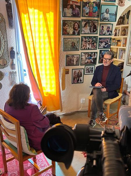 Juan Carlos Gallardo entrevista a Carmen Sarmiento en su casa con una pared llena de fotos de la periodista.