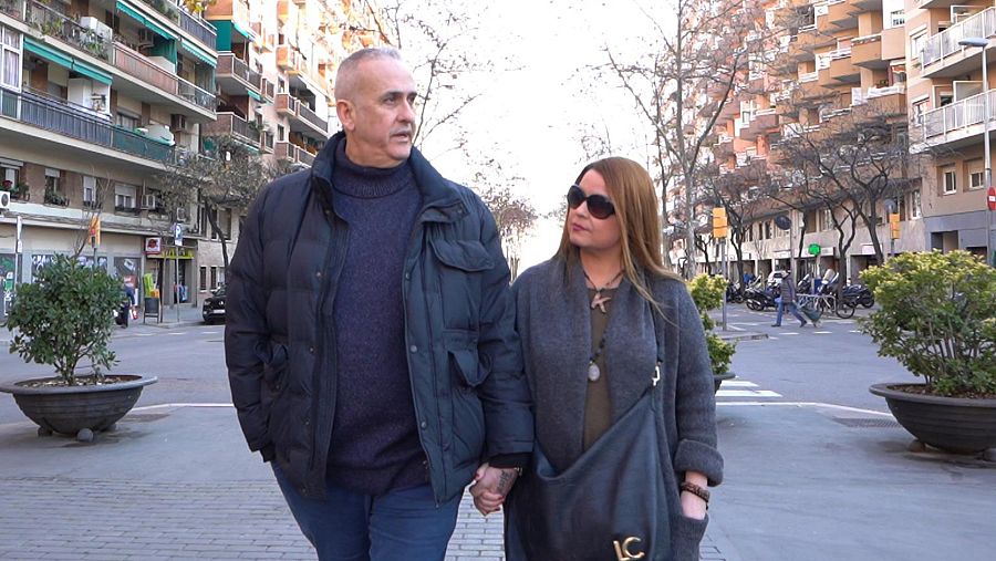 Un hombre y una mujer pasean de frente a la cámara cogidos de la mano por la calle de una ciudad.