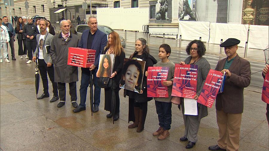 Un grupo de personas posa frente a la cámara cargando con cajas rojas y carteles en una recogida de firmas contra el acoso escolar.