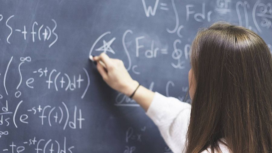 Mujer de espaldas resolviendo una ecuación en una pizarra