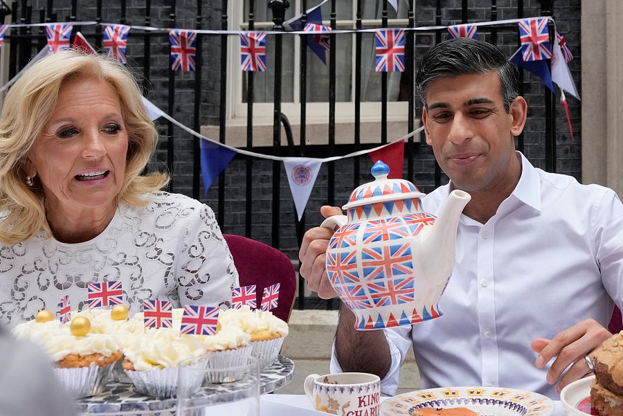 El primer ministro, Rishi Sunak, sostiene una tetera de gran tamaño mientras se sirve una taza sentado junto a la primera dama de EE.UU., Jill Biden, en el Gran Almuerzo celebrado en Downing Street.