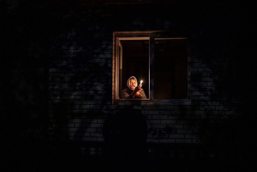 Catherine, de 70 años, mira por la ventana con una vela para alumbrarse en su casa durante un apagón, en Borodyanka, región de Kiev.