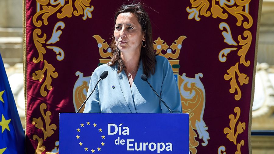 Mujer vestida de azul claro tras atril con leyenda 