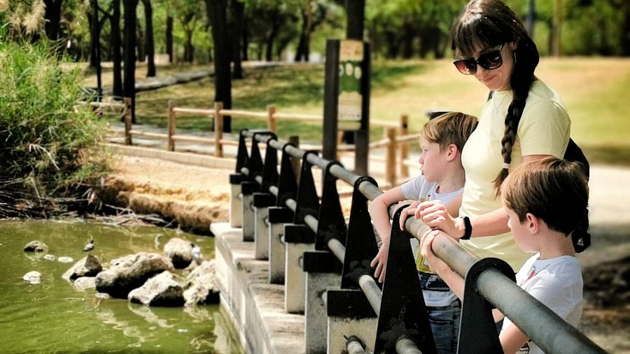 Una mujer y dos niños en un puente sobre el estanque de un parque.