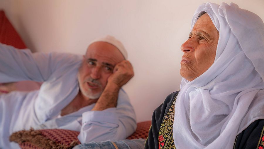 Una mujer y un hombre de rostro árabe. Ella en primer plano y él desenfocado más atrás.