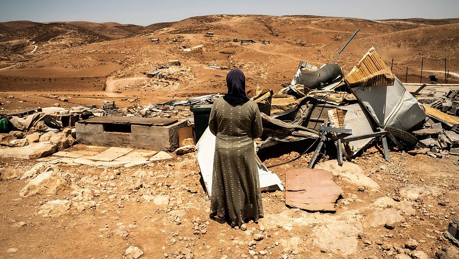 Una mujer de espaldas frente a unas ruinas en mitad del desierto.