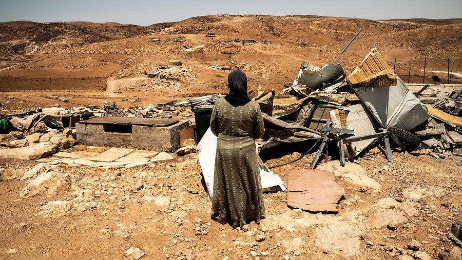 Una mujer de espaldas frente a unas ruinas en mitad del desierto.