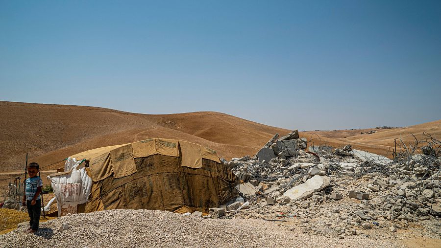 Un niño junto a una tienda de campaña y unas ruinas en el desierto.