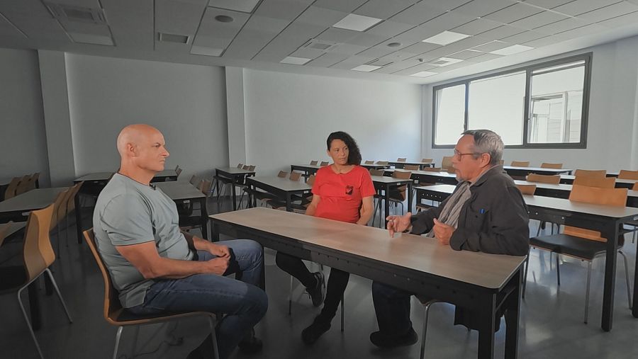 Tres personas sentadas en un aula universitaria conversando.