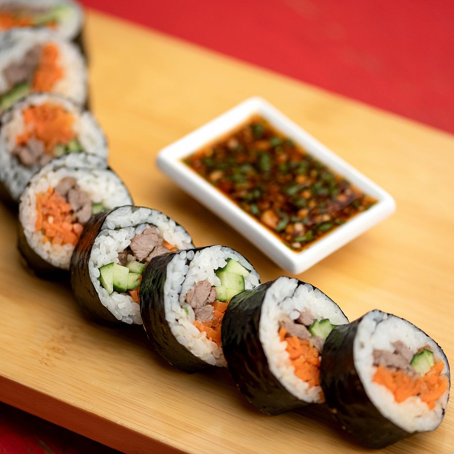 Sushi rolls with beef and vegetables on table. Gravy boat with sauce and fresh herbs. Roll supply. Japanese kitchen. Healthy diet. Close-up. Soft focus.