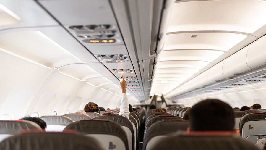 Interior de un avión comercial con algún pasajero sentado en sus asientos