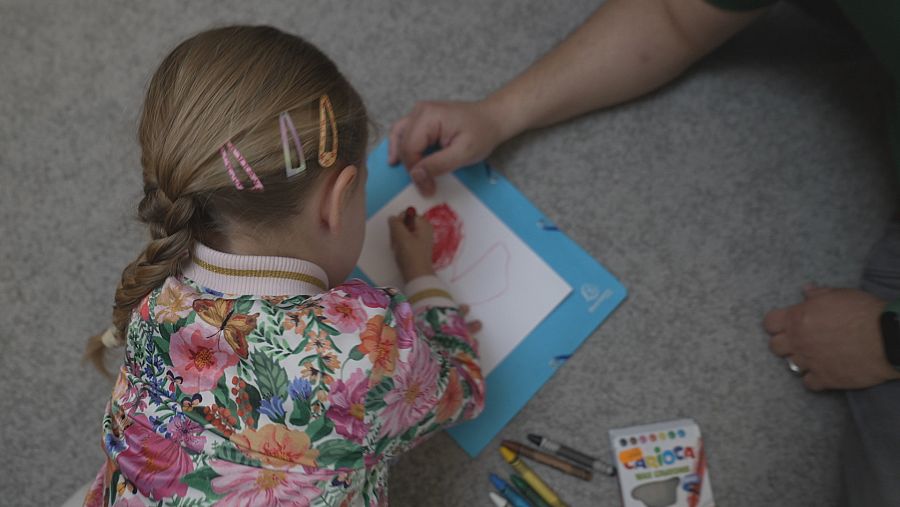 Una niña arrodillada en el suelo pinta un dibujo