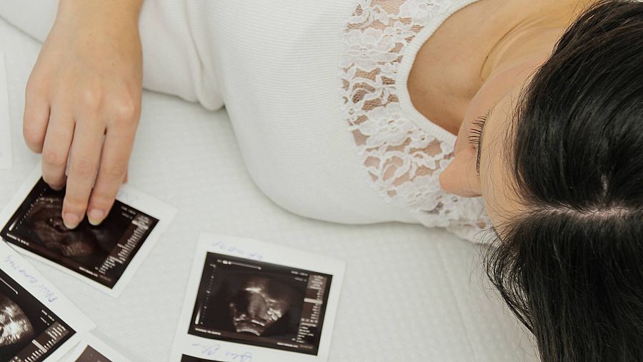 Una mujer mira las ecografías de su bebé no nacido encima de la cama