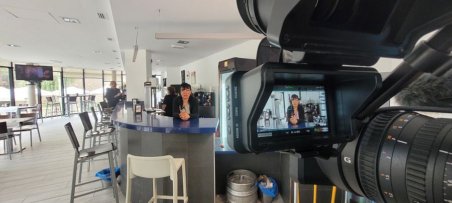 Una mujer detrás de una barra de bar y, en primer plano, la misma mujer en la pantalla de un monitor de grabación