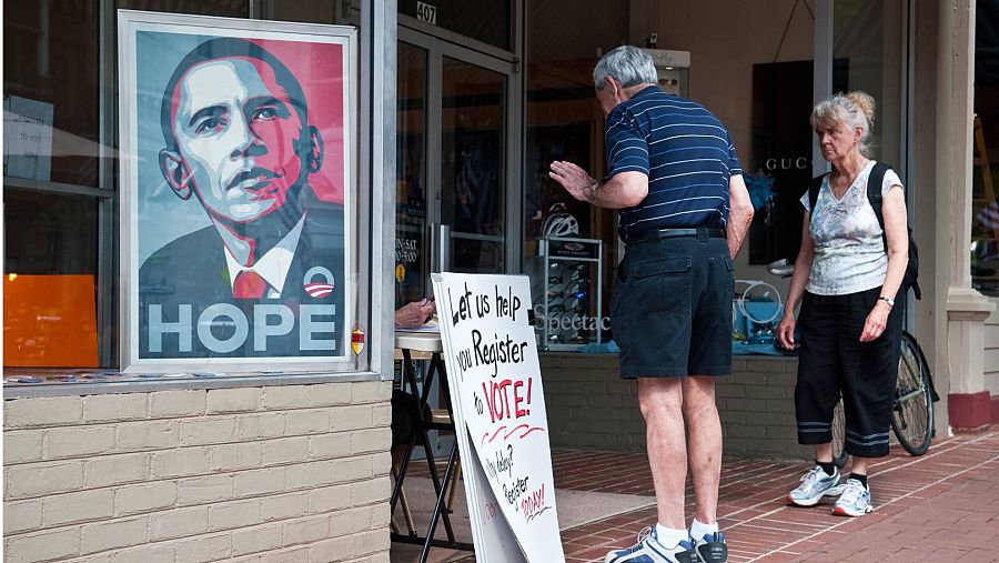 Un cartel con la cara de Obama en un escaparate junto a dos personas