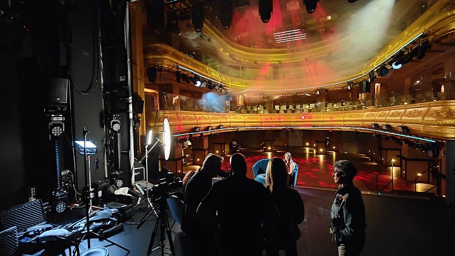 Un equipo de televisión prepara una entrevista en el escenario de un teatro.