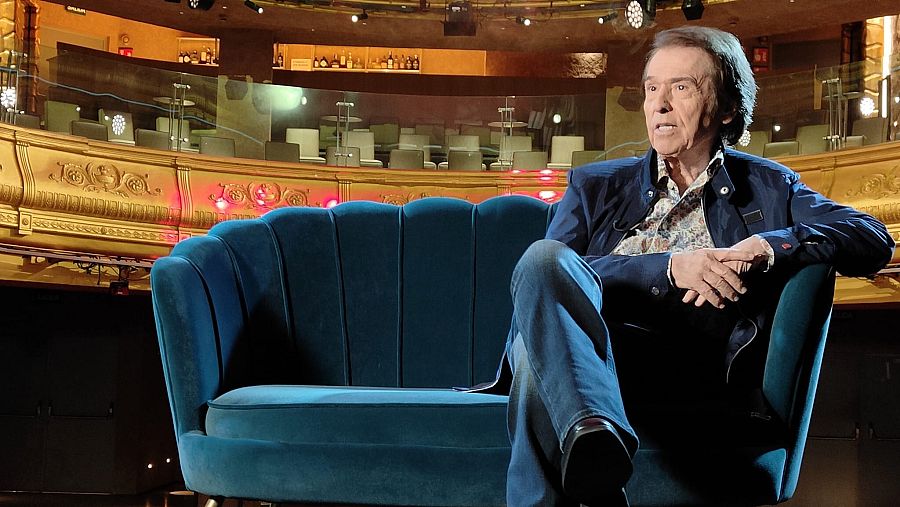 Hombre de negro sentado en un sillón azul con patio de butacas detrás