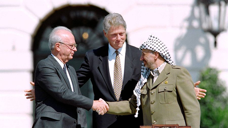 Bill Clinton en el centro de la imagen con los brazos abiertos acoge el apretón de manos de Isaac Rabin y Yasser Arafat, en los Acuerdos de Oslo de 1993.