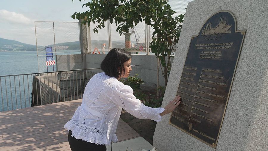 Una mujer inclinada frente a un monolito conmemorativo de piedra con una placa.