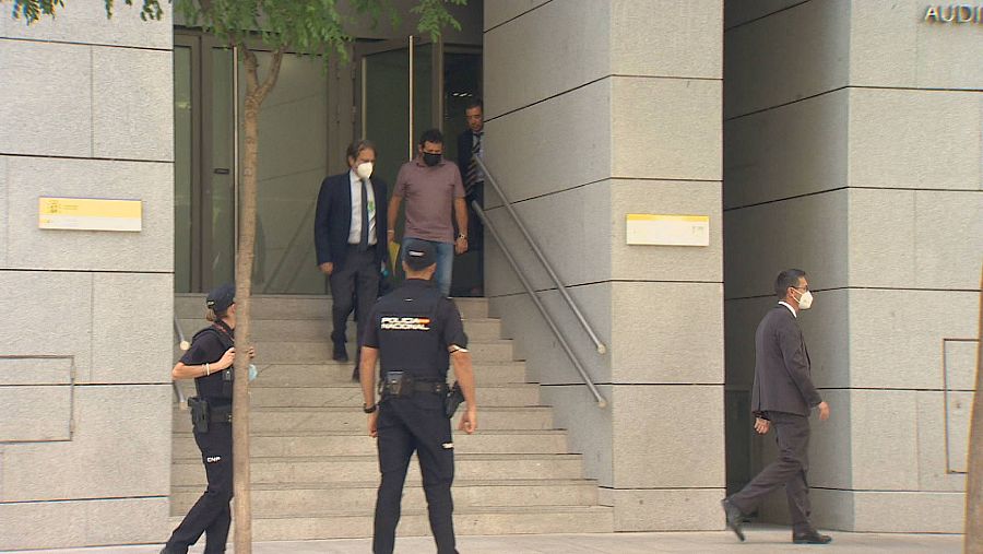 Dos personas con mascarilla bajan unas escaleras en las que se ve a dos policías vestidos de azul.