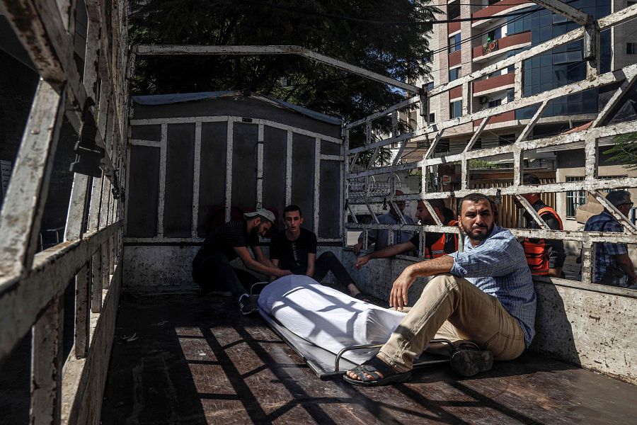 Palestinos sentados junto al cuerpo de uno de los fallecidos en Gaza.