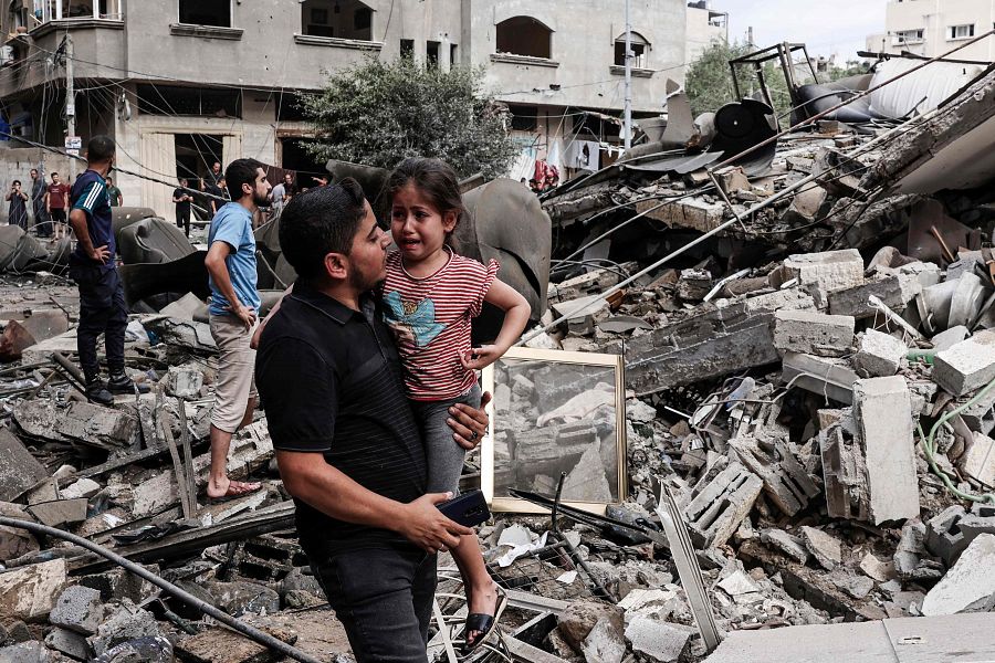 Un hombre sostiene en brazos a una niña entre las ruinas de un edificio bombardeado en la Franja