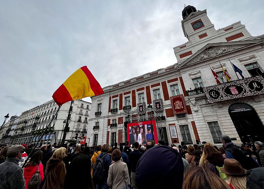 Ciudadanos con banderas ven en las pantallas que se han instalado en la Puerta del Sol la jura de la Constitución de la princesa de Asturias
