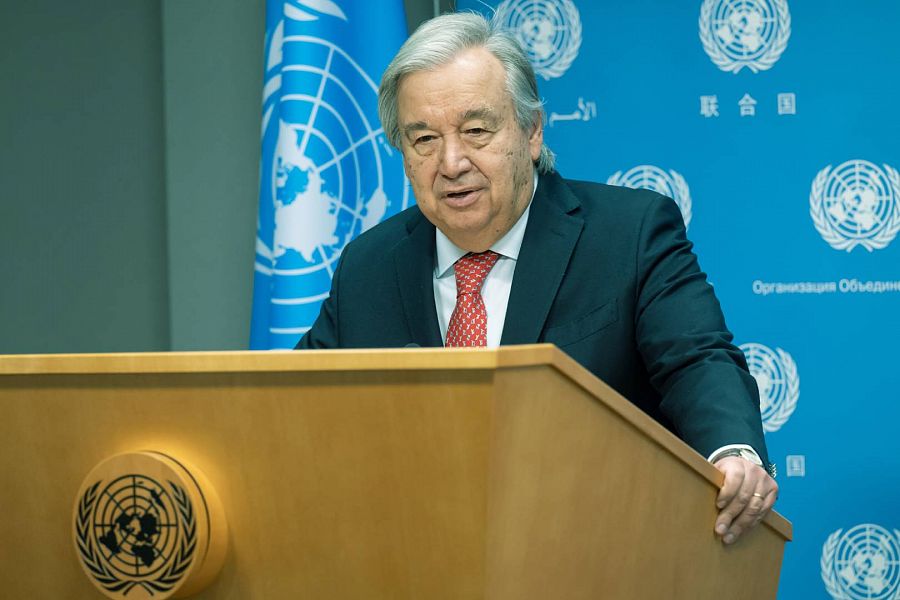 Antonio Guterres se apoya sobre un atril de madera que tiene el símbolo de Naciones Unidas. El logo se repite en el fondo. A un lado, la bandera , también azul.