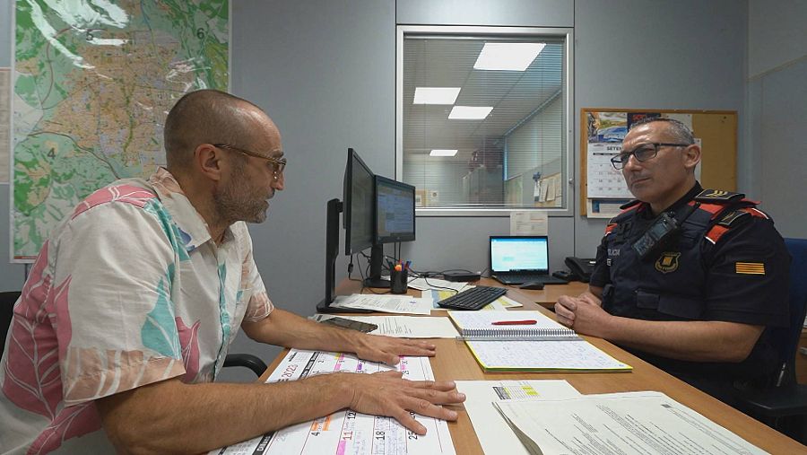 Un hombre conversa en una habitación con un policía, uno a cada lado de una mesa.