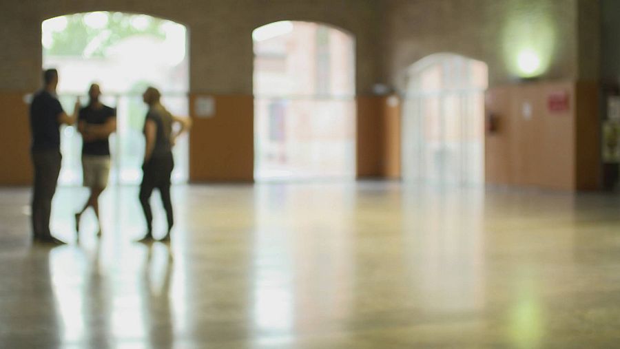 Tres hombres desenfocados en un gran espacio vacío con ventanales.