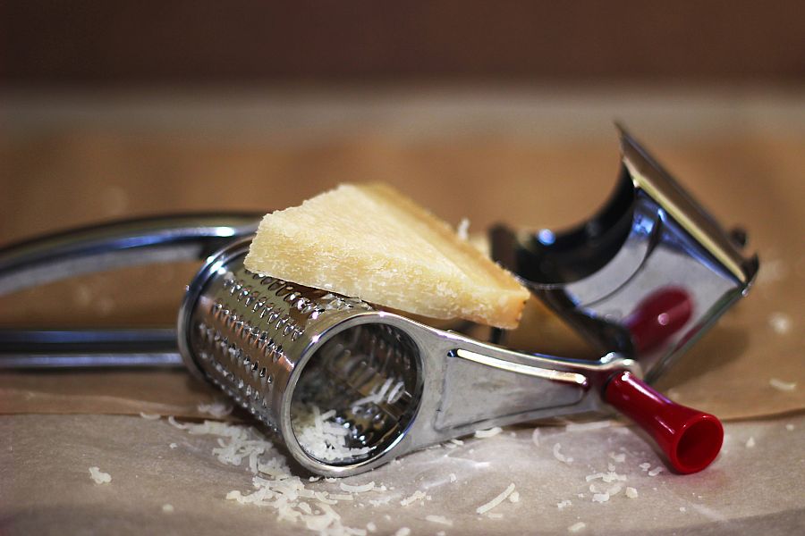 triangular parmesan cheese close-up on brown parchment with grated cheese on a mechanical grater for cheese