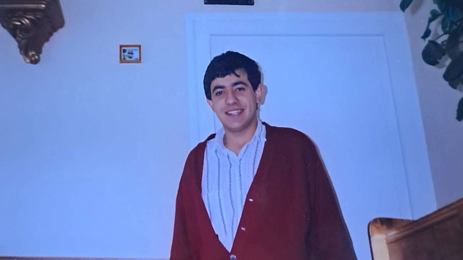 Un adolescente posa de pie dentro de una vivienda.