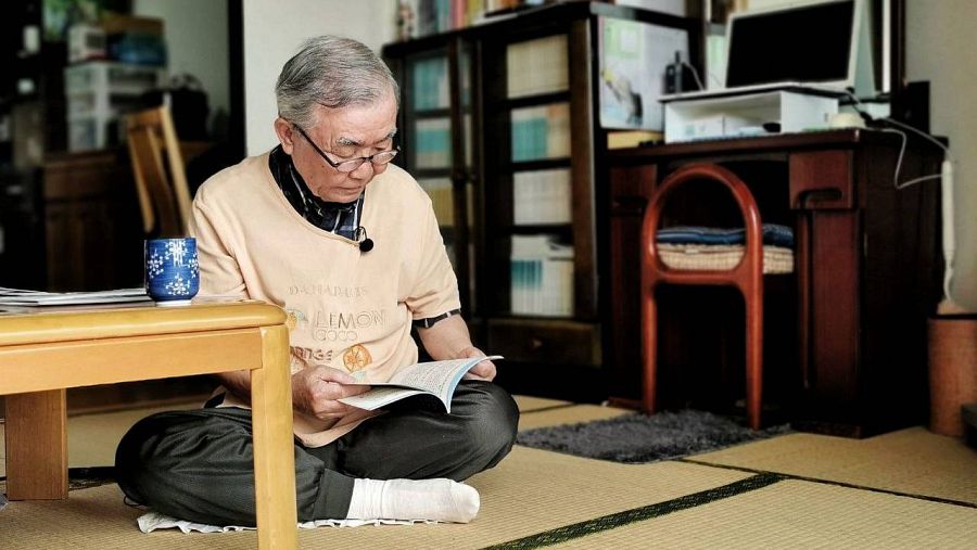 Un anciano japonés sentado en el suelo en el salon de su casa