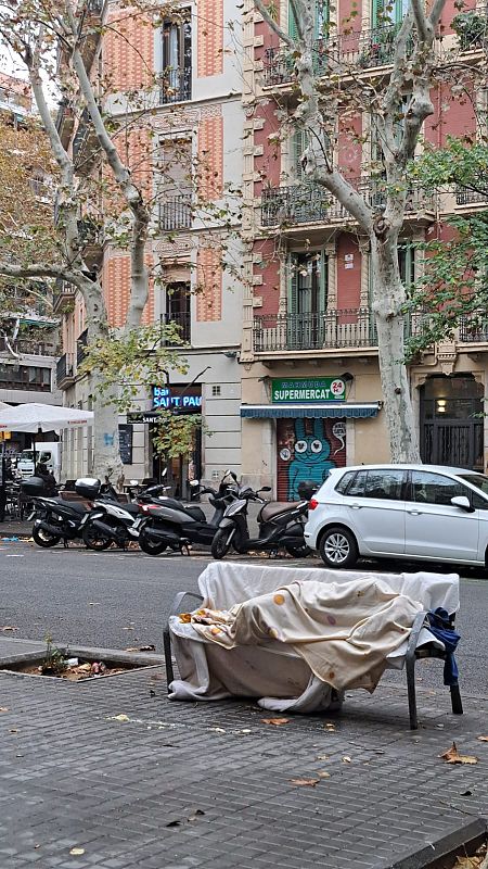 Una persona duerme en un banco de la calle completamente arropada para combatir el frío.