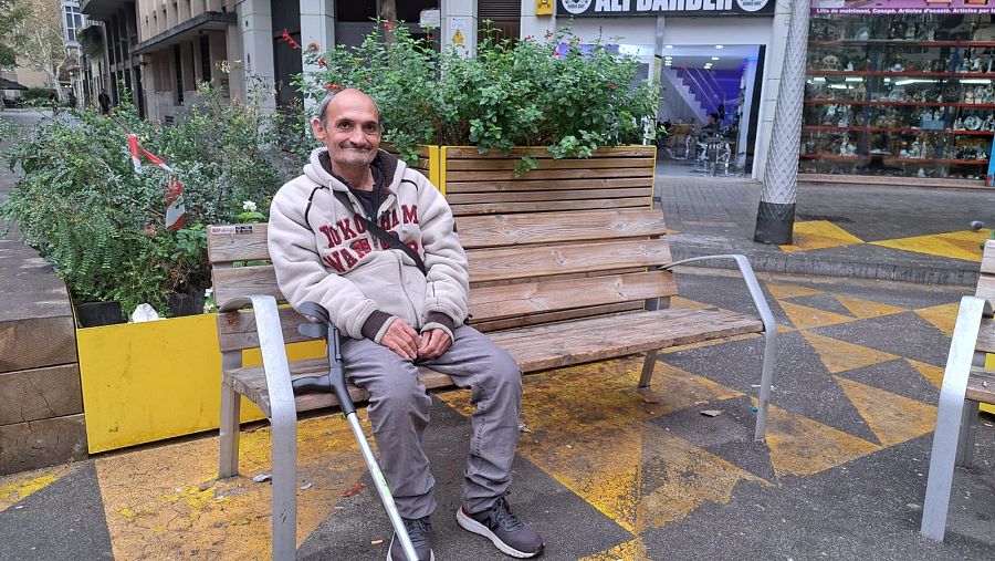 Un hombre sentado en un banco con muchos enseres al lado.