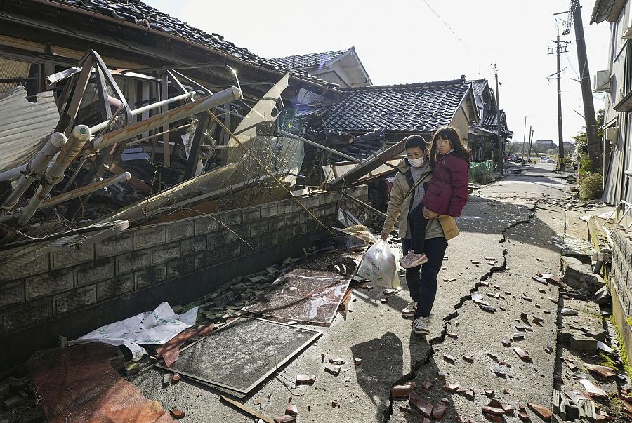 Un hombre con una niña en sus brazos camina entre casas derrumbadas en Suzu, Ishikawa