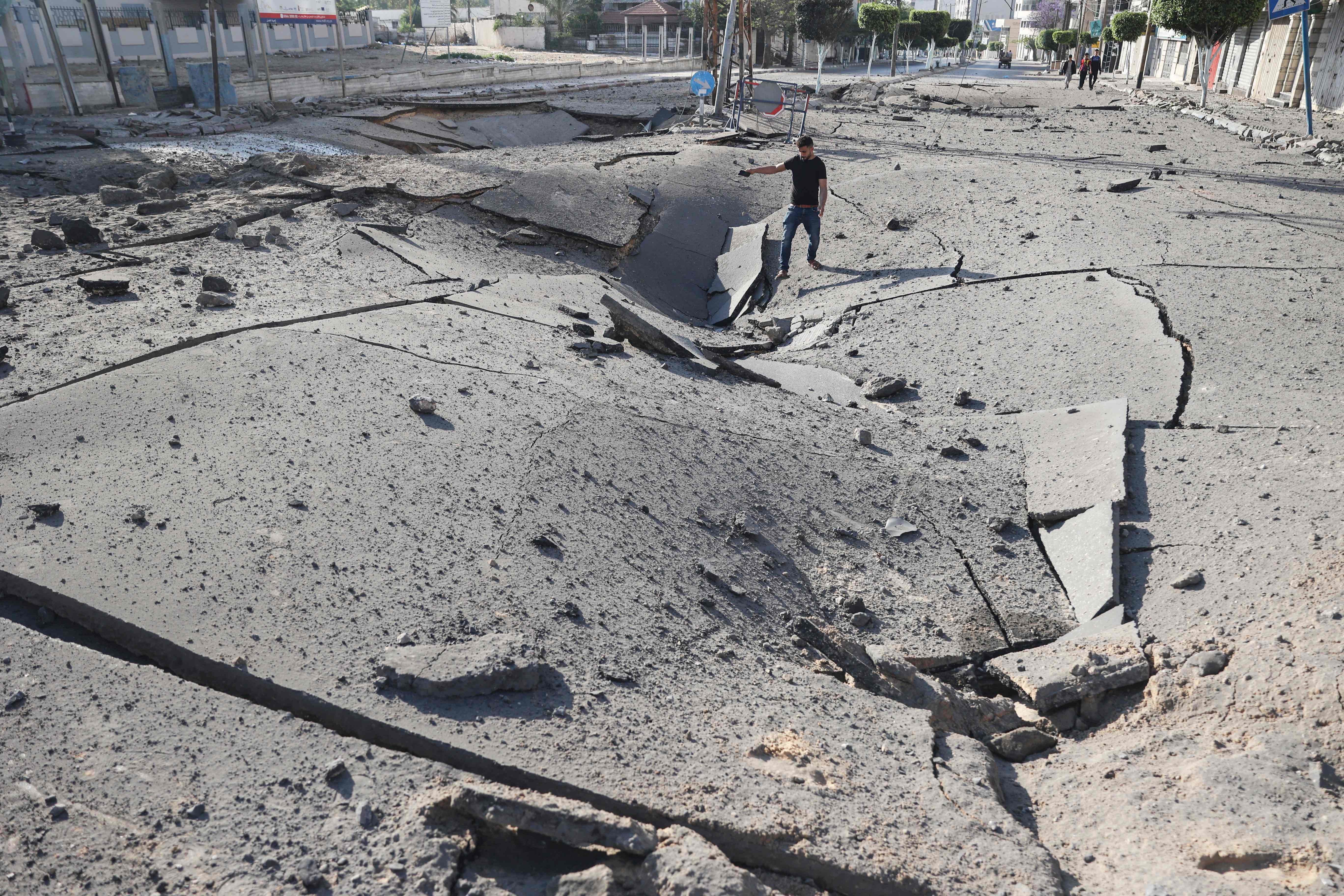 Un joven palestino toma fotografías con su smarthone de un enorme cráter en una carretera principal en la ciudad de Gaza.