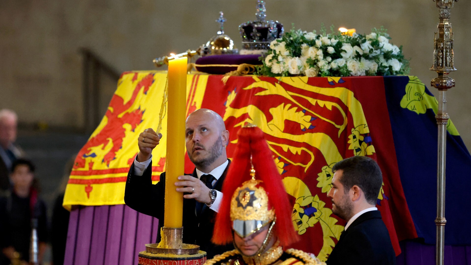 Una persona retira restos de cera de una vela frente al féretro de Isabel II