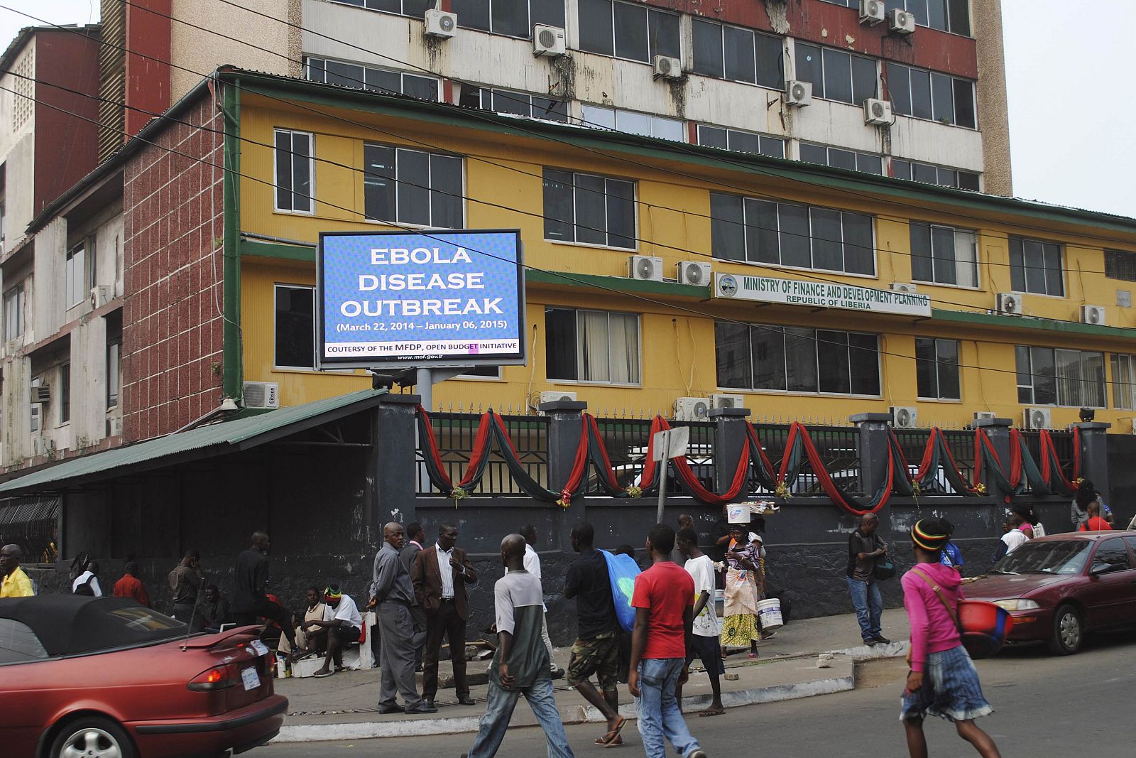 Pedestrians walk past a sign reading "Ebola disease outbreak" outside the Ministry of Finance in Monrovia