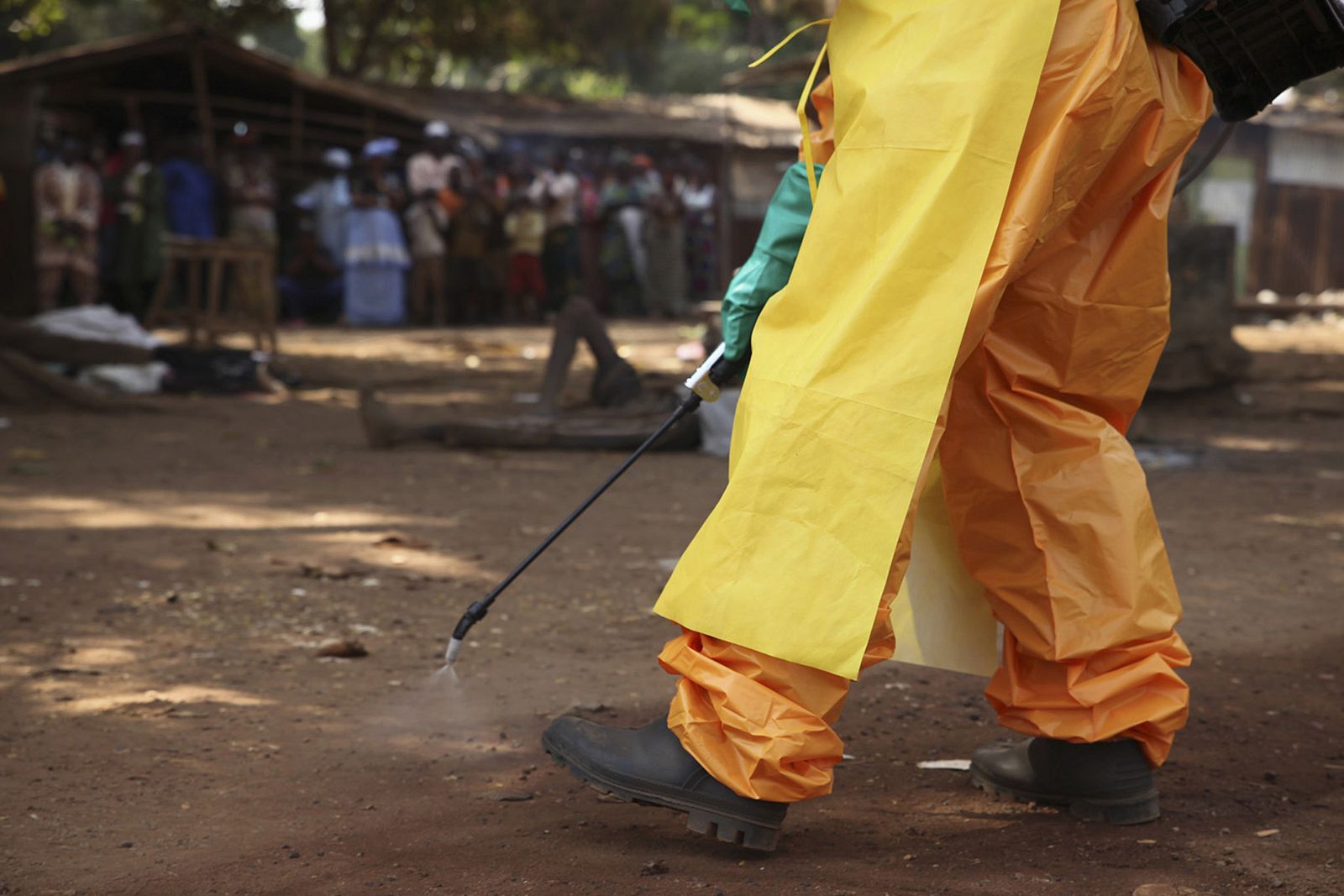 A member of the French Red Cross disinfects the area around a motionless person suspected of carrying the Ebola virus as a crowd gathers in Forecariah