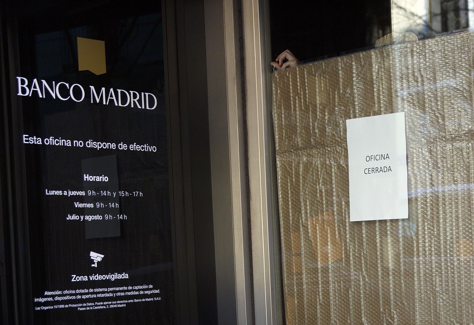 Un empleado cubre la entrada de la sede del Banco Madrid