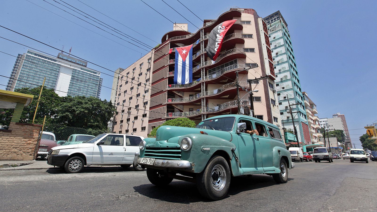 Un auto pasa frente a un edificio donde se expone la bandera cubana y la del movimiento del 26 julio. EFE/Ernesto Mastrascusa