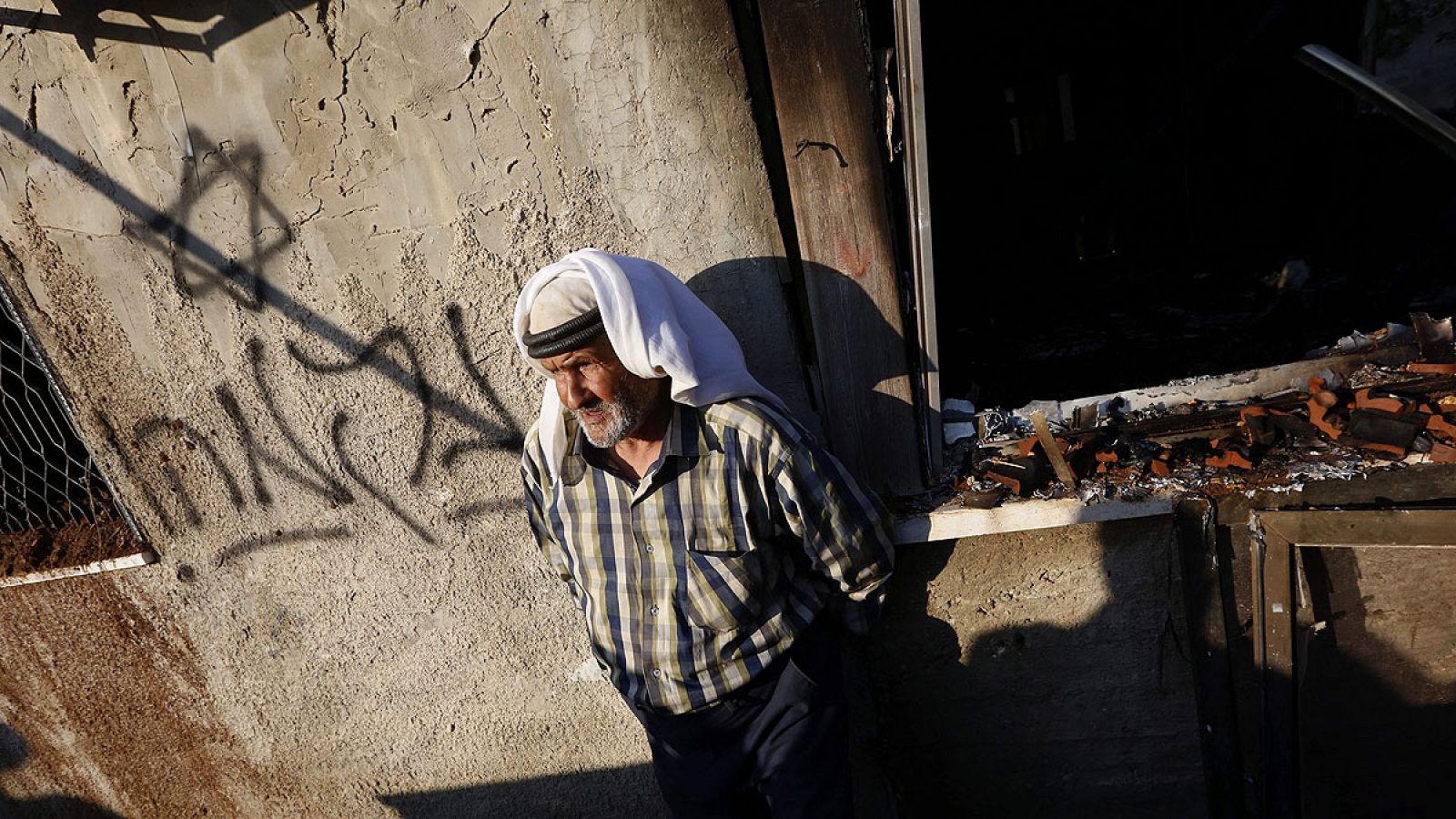 Un familiar de la víctima junto a la casa quemada en Douma, donde los atacantes han escrito "venganza" en hebreo