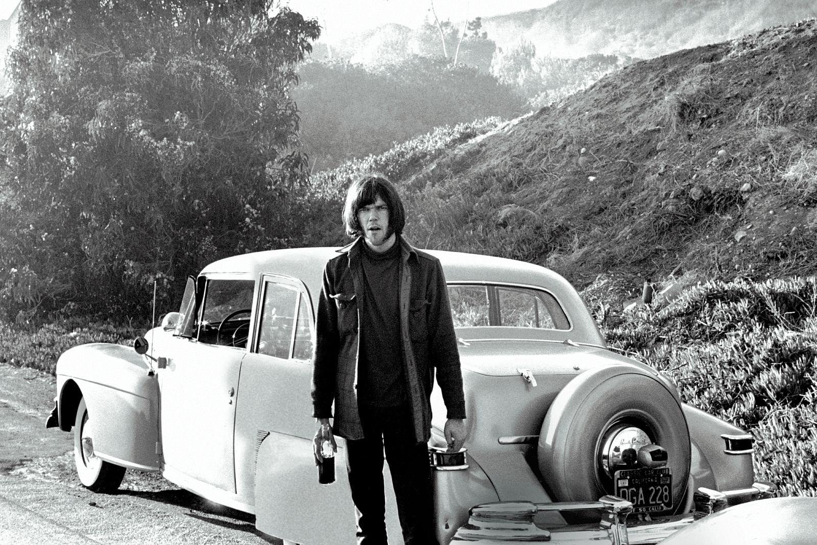 Neil Young fotografiado en Los Ángeles en 1976, junto a uno de los coches de los que habla en 'Super Deluxe: Mi vida al volante'