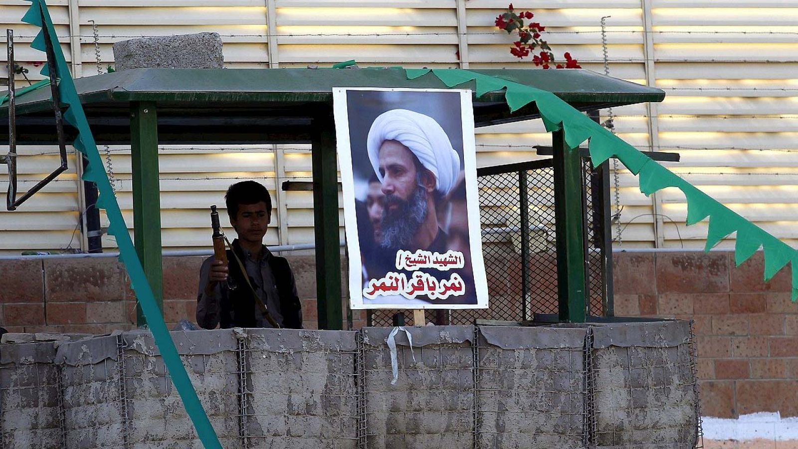 Un miembro de las fuerzas rebeldes de los hutíes hace guardia junto un poster del fallecido clérigo chií Nimr al-Nimr durante una manifestación contra Arabia Saudí organizada frente a la embajada saudita en Saná (Yemen)